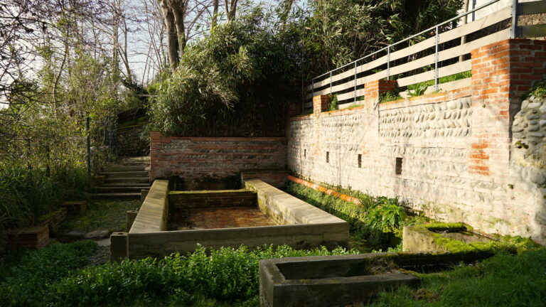 Mur en briques avec un banc en pierre et une fontaine, situ&eacute; pr&egrave;s de la Garonne, accessible par un chemin pentu.